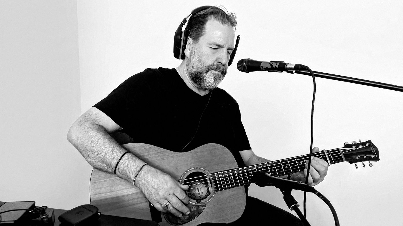 Arnold Rutjens zingt en speelt gitaar achter de microfoon
